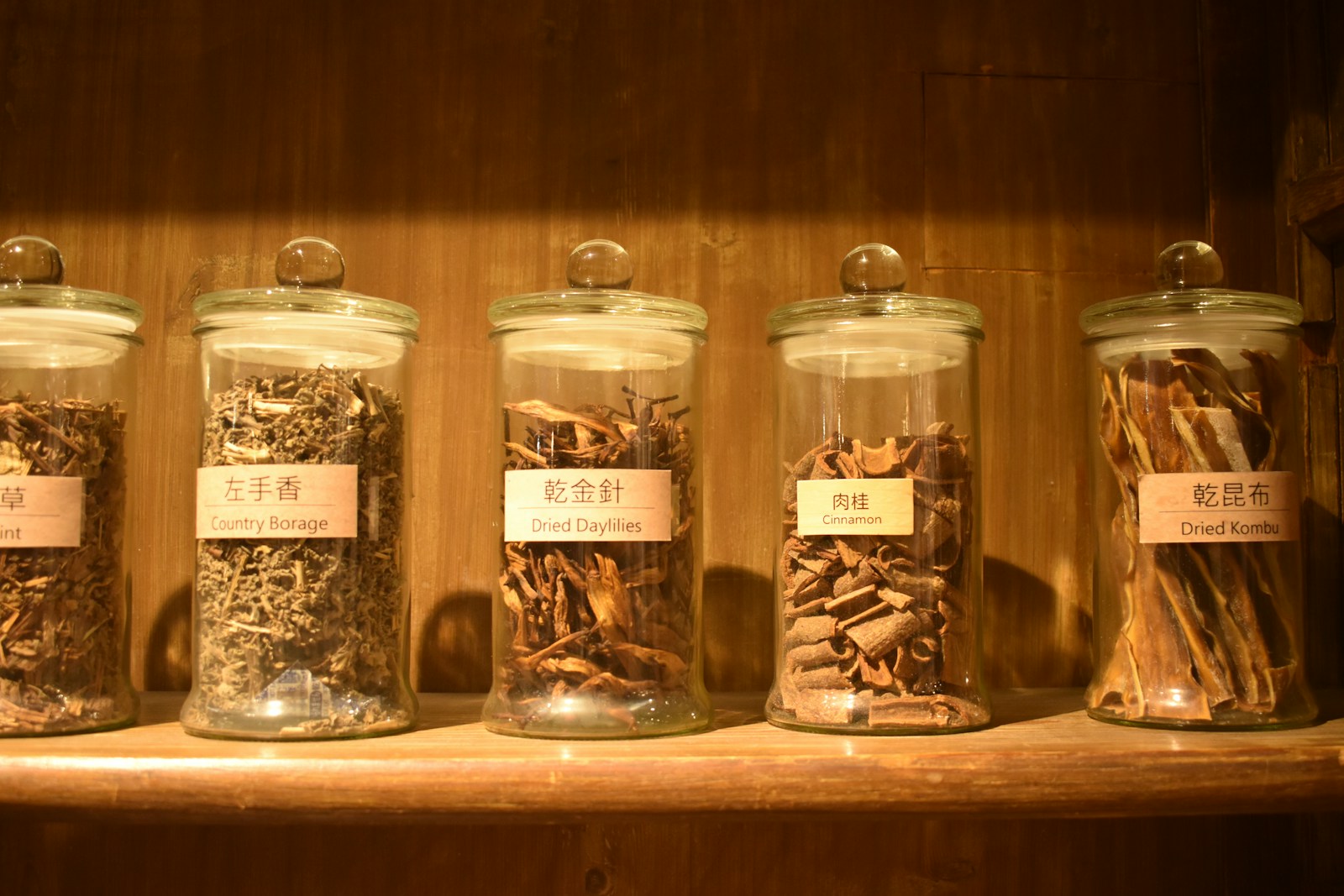 Glass jars of dried herbs, including cinnamon, on a wooden shelf